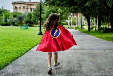 Girl running through the park with a cape